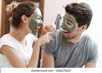 Image of young couple man and woman smiling while standing in bathroom with face mask