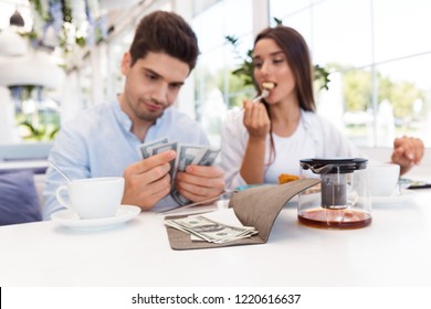 Image of a young displeased confused loving couple sitting in cafe holding check and money. Stock Photo