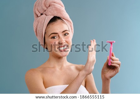 Image of a young displeased woman in towel holding blade and showing no gesture over blue wall background
