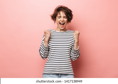 Image of young happy beautiful woman posing isolated over pink wall background make winner gesture.