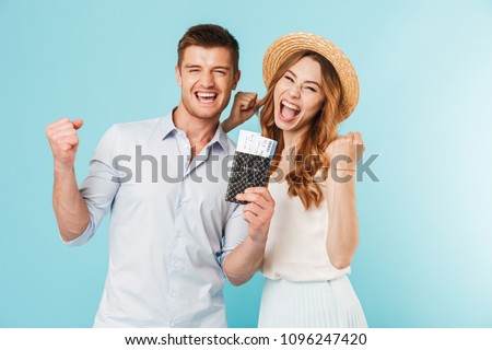 Image of young happy caucasian loving couple isolated over blue background holding passport with tickets make winer gesture.