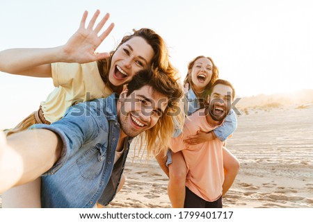 Image of young happy caucasian people smiling and taking selfie photo while walking on beach in summertime