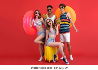 Image Of Young Happy Group Of Friends Standing Isolated Over Red Background. Looking At Camera Holding Cocktails And Rubber Rings.