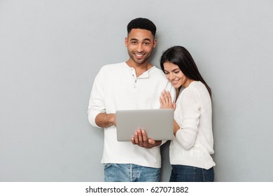 Image Of Young Happy Loving Couple Standing Over Grey Wall And Chatting By Laptop Computer.