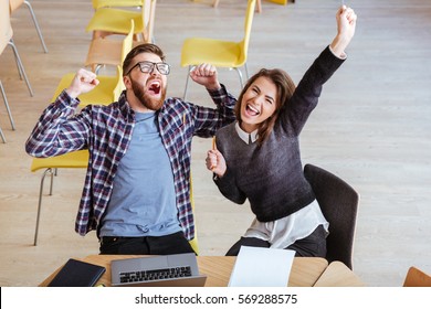 Image Of Young Happy Students Sitting In Library While Make A Winner Gesture.