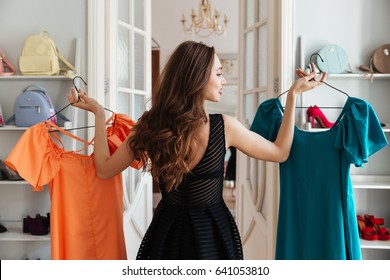 Image of young lady standing in clothes shop indoors choosing dresses. Looking aside. - Shutterstock ID 641053810