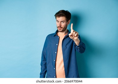 Image of young man give warning, teaching a lesson, raising one finger to scold, looking at camera, patronizing someone, standing on blue background - Shutterstock ID 2066970044