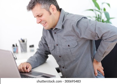 Image Of A Young Man Having A Back Pain While Sitting At The Working Desk