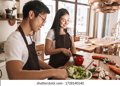 Image of young multicultural couple in aprons laughing and making lunch at cozy kitchen - Powered by Shutterstock