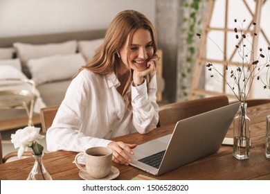 Image young pleased happy cheerful cute beautiful business woman sit indoors in office using laptop computer listening music and earphones 