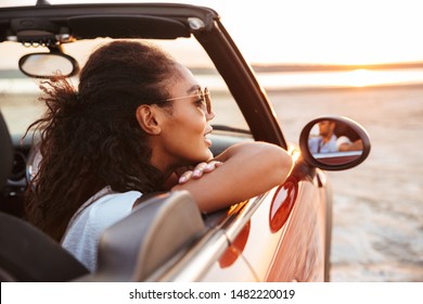 Image Of Young Pretty Woman Smiling And Looking Aside While Riding In Convertible Stylish Car By Seaside