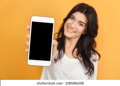 Image of young pretty woman standing isolated over yellow background looking camera showing display of mobile phone.