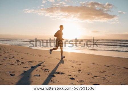 Image of young runner running in morning along the beach. Young man jogging on the sea shore at sunrise.