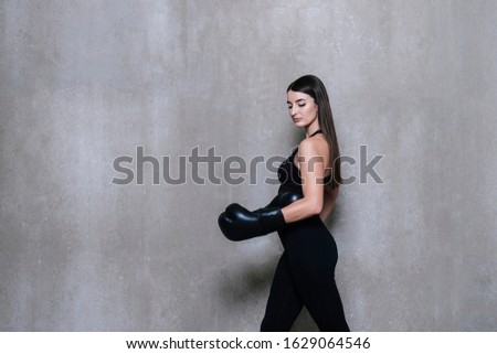 Image of young sports woman in tracksuit and black putting hands together in boxing gloves isolated over grey background