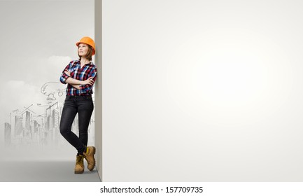 Image of young woman builder wearing helmet and leaning on blank wall