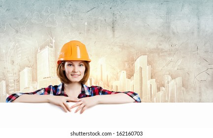 Image of young woman builder wearing helmet and holding blank banner