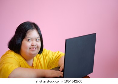 Image of a young woman with Down syndrome or a cerebral palsy student working and learning with laptop Pink background