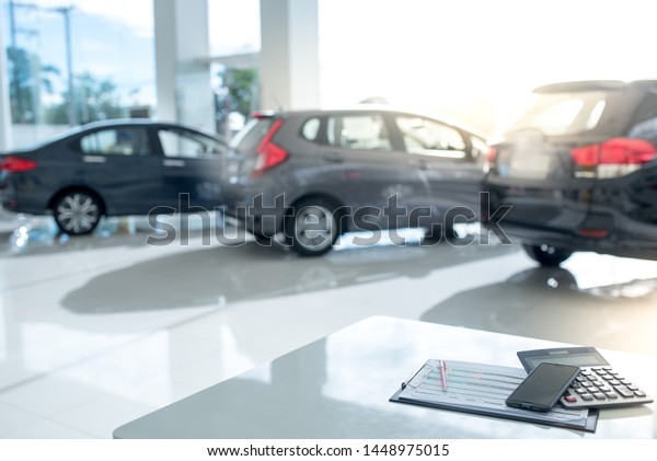 Images in a car showroom with calculators\
and smartphones placed on a table in the workplace in a new car\
showroom. The background is a car\
showroom.
