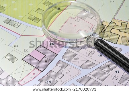 Imaginary cadastral map with buildings, land parcel and vacant plot - property registry and real estate concept seen through a magnifying glass