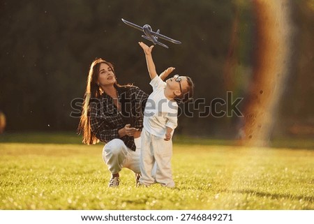 Imagination conception, playing with toy plane. Mother and son together in an open field during daytime.