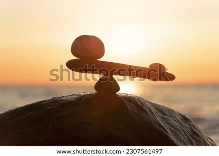 Imbalance of forces - natural scales of stones ( in imbalance) at the sea to the orange sunset - symbol photo	