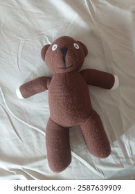 Imitation of Mr. Bean's Teddy Bear. The teddy bear is brown, laying above messy bed sheet. 