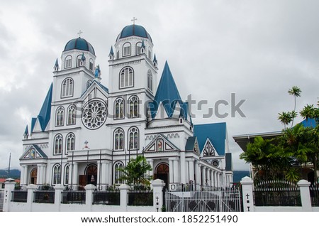 The Immaculate Conception Cathedral surrounded by plants under a cloudy sky in Apia, Samoa