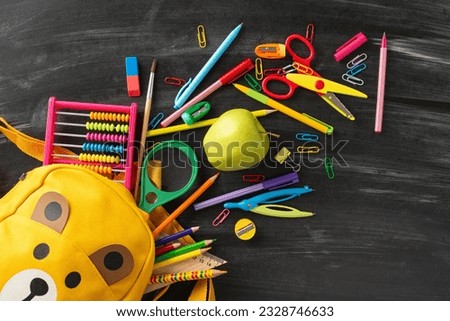 Immerse yourself in educational process with this top-view photo of kid's yellow school bag, snack for lunch and stationery like abacus, pen, pencils ant other items on isolated blackboard background