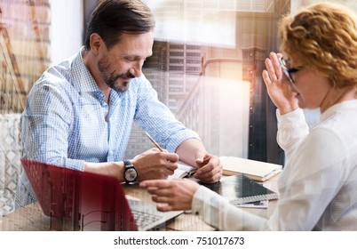 Immersed into work. Pleasant middle-aged colleagues sitting at the table and working on a new report together while the man making notes and the woman explaining her stance - Shutterstock ID 751017673