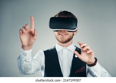 Immersed In A Virtual Business Environment. Studio Shot Of A Handsome Young Businessman Using A Vr Headset Against A Grey Background.