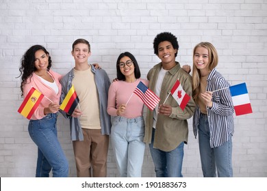 Immigrants of different countries and exchange students in language school. Smiling multiracial young people hold flags of France, Canada, USA, Germany and Spanish in classroom, studio shot