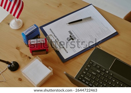 Immigration application being processed on office desk with stamps and pen. American flag in background with laptop and forms present on workspace