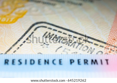 Immigration concept image. Residence permit card over immigration stamp on UK visa in passport. Selective focus