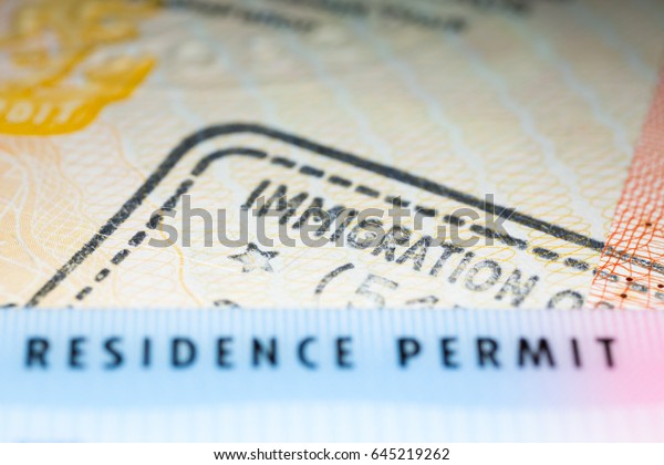 Immigration concept\
image. Residence permit card over immigration stamp on UK visa in\
passport. Selective\
focus