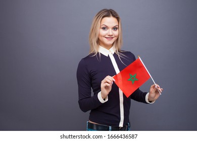 Immigration and the study of foreign languages, concept. A young smiling woman with a Morocco flag in her hand. Girl waving a Moroccan flag on a gray background