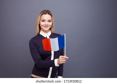 Immigration And The Study Of Foreign Languages, Concept. A Young Smiling Woman With A France Flag In Her Hand. Girl Waving A French Flag On A Gray Background