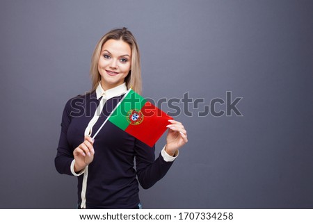 Immigration and the study of foreign languages, concept. A young smiling woman with a Portugal flag in her hand. Girl waving a Portuguese flag on a gray background