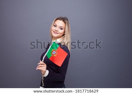 Immigration and the study of foreign languages, concept. A young smiling woman with a Portugal flag in her hand. woman waving a Portuguese flag on a gray background