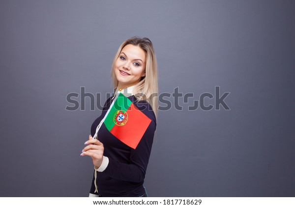 Immigration and the study of foreign\
languages, concept. A young smiling woman with a Portugal flag in\
her hand. woman waving a Portuguese flag on a gray\
background