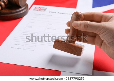 Immigration to United Kingdom. Woman stamping visa application form on flag, closeup