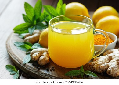 Immune booster antivirus drink, turmeric with ginger, lemon, mint and spices hot winter tea on wooden rustic background, closeup, natural medicine and naturopathy concept - Shutterstock ID 2064235286