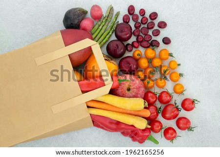 Immune boosting fruit and  vegetables for good health high in lycopene, anthocyanins, antioxidants, vitamins, minerals and dietary fibre. In a paper carrier bag and loose on mottled grey background.  