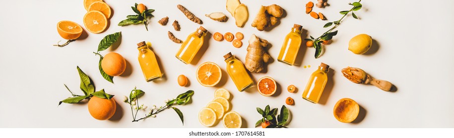 Immune boosting natural vitamin health defending drink. Flat-lay of fresh turmeric, ginger and citrus juice shots over white background, top view, wide composition. Vegan Immunity system booster