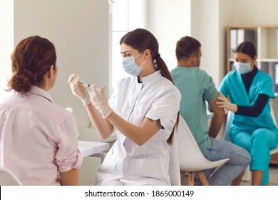 Immunization campaign and mass vaccination concept. Concentrated young nurse in face mask getting vaccine ready for injection. Diverse doctors and medical workers giving people Covid-19 or flu shots