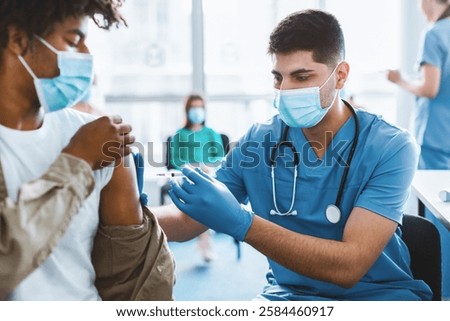 Immunization, Prevention Procedure Concept. Closeup Of African Guy In Surgical Mask Receiving Intramuscular Injection In Arm Getting Shot In Shoulder During Doctor's Appointment In Medical Centre
