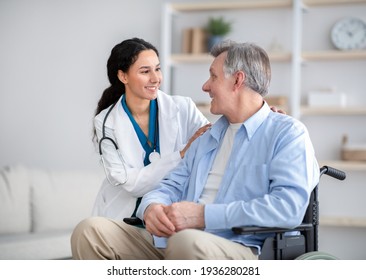 Impaired Senior Man In Wheelchair And Young Nurse Taking Care Of Him At Home