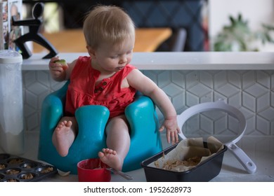 Imperfect Parenting - A Messy Baby Sits On A Kitchen Bench Surrounded By A While Mum Or Dad Tries To Bake To Illustrate What Raising A Baby Is Really Like. Authentic Moment Captured Of My Little Girl.