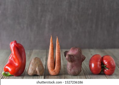 Imperfect red pepper, carrot,  sweet potato, red tomato arranged in a row on a wooden background. Food concept, imperfect produce concept.Image with copy space.