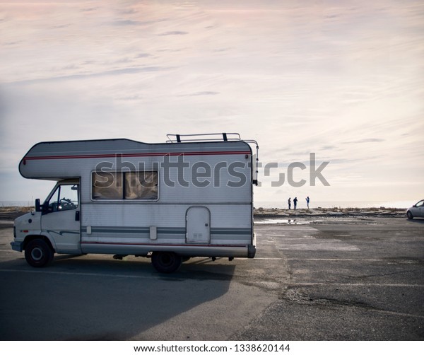 IMPERIA, ITALY - 12/01/2019: Group of young people\
taking pictures and having fun in beach with camping caravanning\
motor home mobile home parked. Mediterranean europe road trip\
tourism. Coastal town.