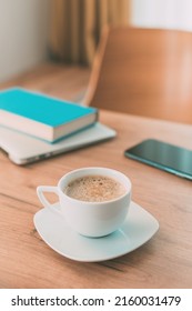 Importance of caffeine and coffee for freelance work. Coffee cup, mobile smart phone, laptop computer and a book on home office table. - Shutterstock ID 2160031479